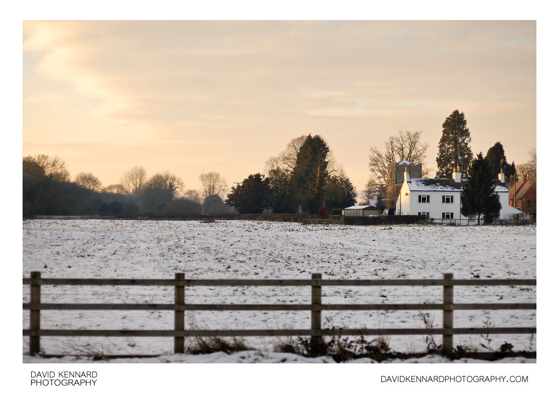 Snowy field and white house at sunset