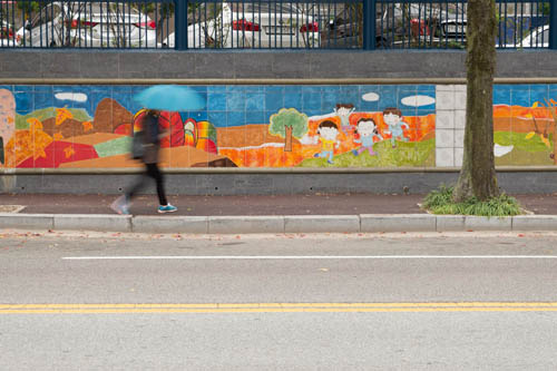 Woman with a blue umbrella walking past a colourfully painted wall in Gwangju, South Korea